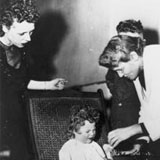 Helen Taussig examining a child, her large boxed hearing aid is next to the child, ca. 1947