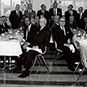 Diverse group of well dressed men sitting at two lunch tables.