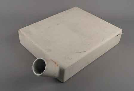 Square-sided, flat ceramic vessel with short cylindrical spout near one corner.