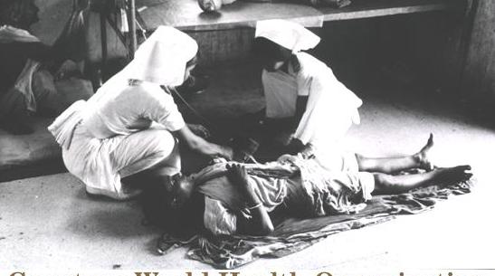Interior view: two nurses attach an intravenous drip containing rehydration fluids to a female patient lying on the floor; two other female patients are present.