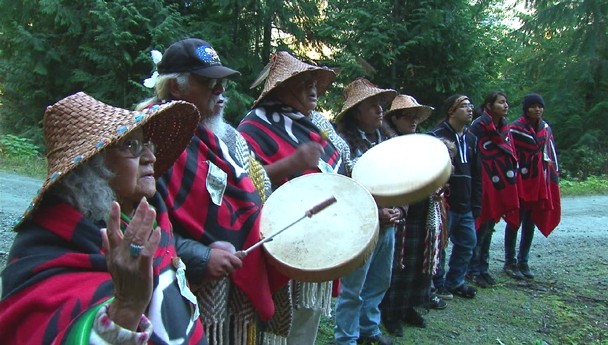 Color image of several Native individuals standing in a line while performing a tree blessing ceremony.