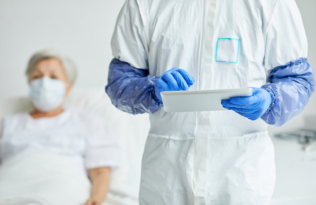 medical professional wearing PPE using tablet with patient in mask in background