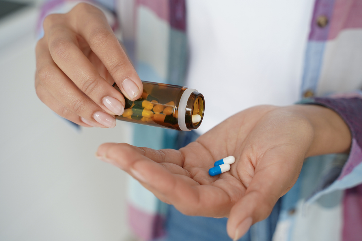 Woman's hands pours medical capsules out of jar into palm